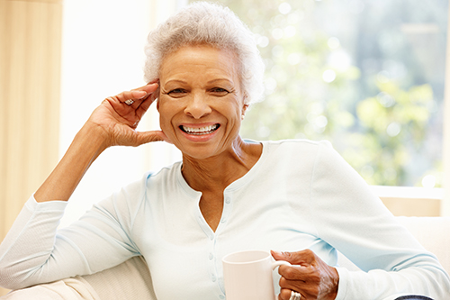 African american woman wearing yellow and holding a coffee cup while sitting on the couch